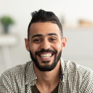 portrait-of-handsome-young-arab-man-smiling-and-looking-at-camera-sitting-on-sofa-at-home-e1687402178567.jpg